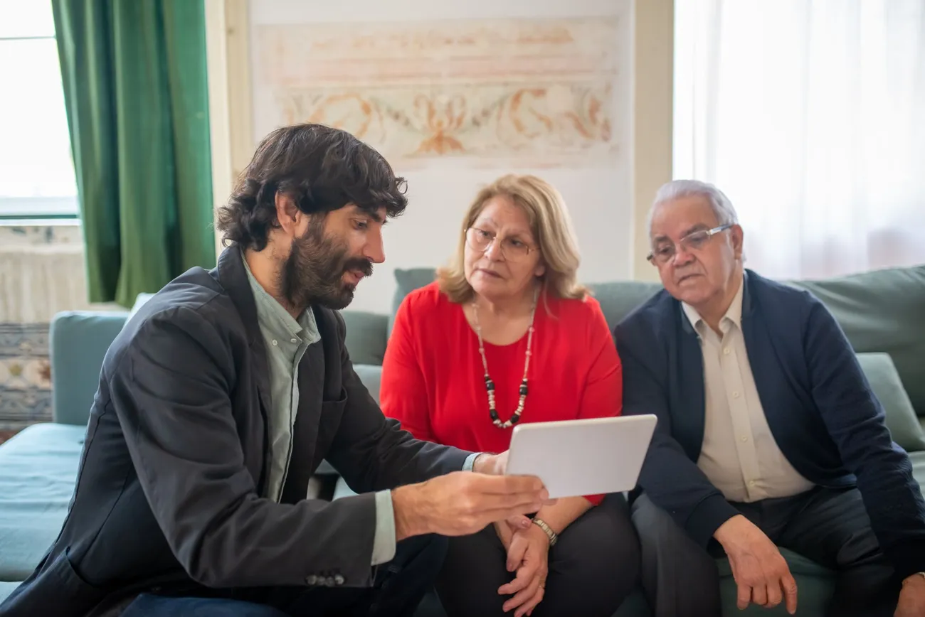 Agente de seguros explicando opciones de Medicare en una tableta a una pareja de adultos mayores en su casa