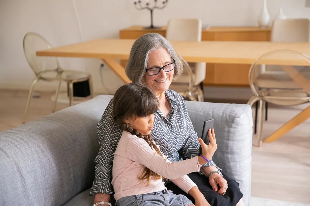 Abuela y nieta sonriendo mientras miran un celular en la sala
